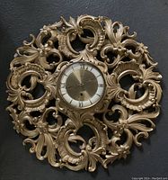Front view of the large ornate vintage Welby wall clock showing detailed scroll and flower design around the clock face with Roman numerals.