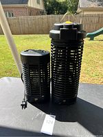 Two black electric bug zappers side by side on a table outdoors with a grassy background.