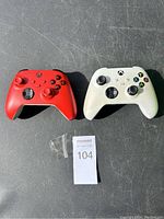 Photo showing both red and white Xbox wireless controllers together on a dark surface.