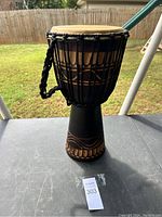 Full view of African djembe drum on table outside, showing entire drum body and drumhead with rope tuning.
