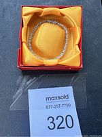 Silver bracelet in box with yellow fabric lining, displayed in a coiled position.