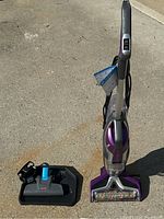 Full view of the Bissell vacuum cleaner standing upright outdoors with attached charging/docking station placed beside it showing accessories and overall condition.
