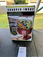 Front view of new Sharper Image motion activated candy dispenser box showing colorful candy inside and highlighting built-in sensor for touchless operation.