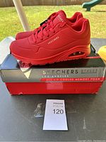 Photo of red Skechers shoes on box outdoors showing the side and top profile with brand and tag visible.