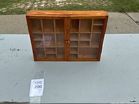 Front view of the compact rectangular wooden curio cabinet with two glass doors closed, showing the natural wood grain and compartments inside.