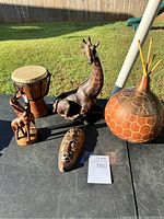 Full view of lot on table with lawn background showing all items including drum, giraffe carvings, buffalo, mask, and decorative gourd