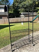 Full view of the black metal rolling rack outside, showing its four wire shelves and caster wheels.