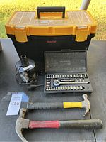 Photo of closed toolbox with hammers, socket set case, and drill attachment displayed in front.