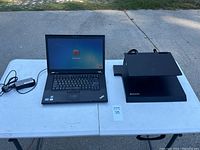 Lenovo ThinkPad T520 laptop, power supply, and Lenovo docking station displayed on folding table outdoors.