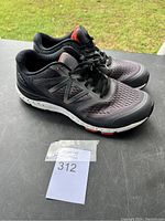 Pair of black and gray New Balance shoes with black laces and orange detailing, shown from the side angle.