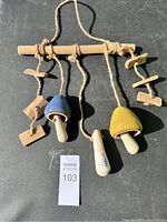Photo of the full wind chime showing two ceramic mushrooms colored blue and yellow hanging from a wooden rod with natural fiber ropes and small wooden pieces.