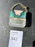 Front view of Marc Jacobs Decadence Eau So Decadent perfume bottle with textured snakeskin cap and gold chain detail.