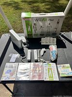 Nintendo Wii console set with accessories and multiple Wii games displayed on table outdoors.