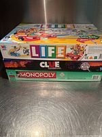 Side view of the three stacked board game boxes showing The Game of Life, Clue, and Monopoly titles and artwork.