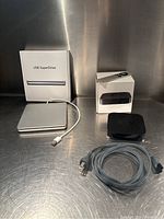 Apple USB SuperDrive box next to external drive unit and cable; Apple TV device, remote control, power cable, and Apple TV box