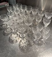 28 pieces of clear cut crystal stemware grouped together on a reflective surface showing various sizes and patterns