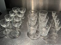 All 19 crystal glasses grouped by type on a metallic surface under bright lighting showing the full set.