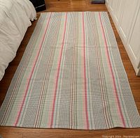 Full view of the flat-woven striped cotton rug laid on hardwood floor showing multicolor narrow stripes in pastel colors