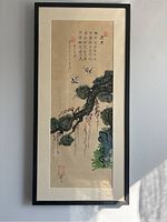Framed vertical Asian scroll painting hung on wall, showing entire artwork including tree, birds, and calligraphy.