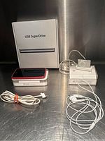 Photo of all items: iPod Touch on its box, USB SuperDrive box behind, iPod Shuffle on its box with earphones, and charging cable laying in front.