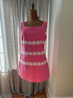 Front view of sleeveless bright pink dress with white lace floral bands displayed on dress form