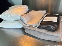 Full view of all bedding items stacked on metallic surface, including white fitted sheet, blue linen covers, and satin pillowcases in packaging.