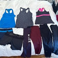 Overview of all clothing items laid out on bed including three tank tops and four bottoms.