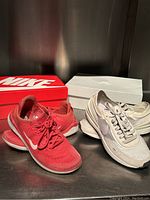 Two pairs of Nike running shoes: one red and one white with a purple swoosh on their respective shoeboxes.