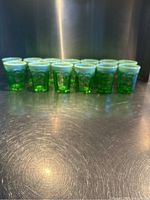 Row of thirteen green pressed glass tumblers with milk glass rims lined up