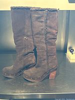 Side view of brown suede boots showing side zipper, fleece trim, wooden block heel, and metal stud accents along sole edge