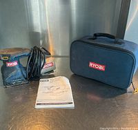 Full view of sander, carrying case, and instruction manual on a metallic surface