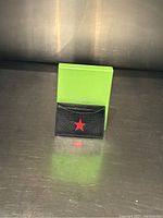 Black leather credit card wallet with a red star in front, placed upright in front of a green box.