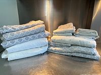 View of folded sheets and pillowcases stacked on a shelf, showing white sheets, sheets with grayish geometric patterns, and sheets with light green polka dots.