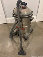 Full view of Shop Vac stainless steel tank with attached black hose and nozzle on floor.