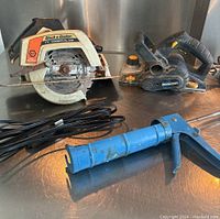 Full lot left side view featuring Black & Decker circular saw, Mastercraft planer, blue caulking gun, and black extension cord on metallic surface.