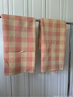 Two vintage pink and creme checkered wool blankets displayed hanging over a rod showing full patterns and colors