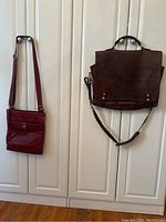 Red leather crossbody bag with front snap pocket and adjustable strap shown hanging beside briefcase