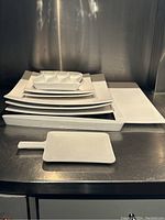 Photo showing the array of white ceramic serving dishes stacked and arranged on stainless steel surface.