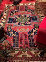 Rug laid flat on red carpeted floor, full view showing central geometric pattern