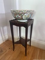 Full front view of porcelain bowl on wood stand against wall.