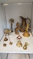 Full view of all brass items arranged on a shelf, showing pitcher, horse, standing man, bird, bell, and hand-shaped holder.