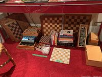 Overview of chess boards, pieces and books on red carpet under shelf