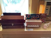 Multiple wooden chess boxes stacked, boxed game sets including magnetic Backgammon, Chess, and Checker, plus a 'Win at Checkers' booklet and ceramic game pieces.