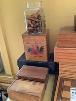 Overview of multiple stacked wooden boxes, decorative box, black case, jar of wooden pieces and partial board visible