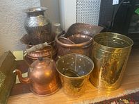 Wide view of assorted copper and brass ware including bucket vessels, kettle, large pot and urn with hammered texture.