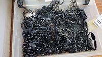 Image showing multiple black necklaces and bracelets tangled together in a clear plastic container.