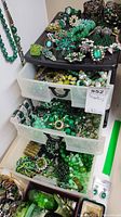 Three-drawer plastic container filled with assorted green-tone costume jewelry