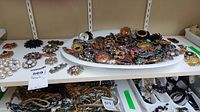Overview of white tray holding a large assortment of brooches on a white table shelf