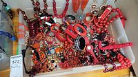 Plastic container filled with assorted red and orange resin and beadwork necklaces, bracelets and bangles