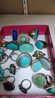 Multiple costume rings in a pink box showcasing a variety of turquoise and green stones and decorative metal bands.